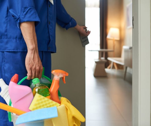 unrecognizable-cleaner-walking-into-hotel-room-with-tools-detergents